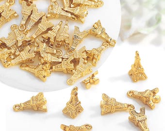 May include: A selection of small, gold-coloured Eiffel Tower charms. The charms are intricately detailed, with visible architectural features. Each charm has a small loop for attaching to jewellery or other crafts. The charms are scattered on a white surface.