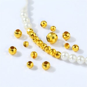May include: A close-up of gold-colored faceted beads. The beads are scattered on a white surface. Some of the beads are strung on a white string.
