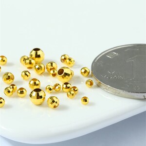 May include: A close-up of a group of small, gold-colored metal beads. The beads are faceted and have a hole in the center. A Chinese yuan coin is in the background for size reference.