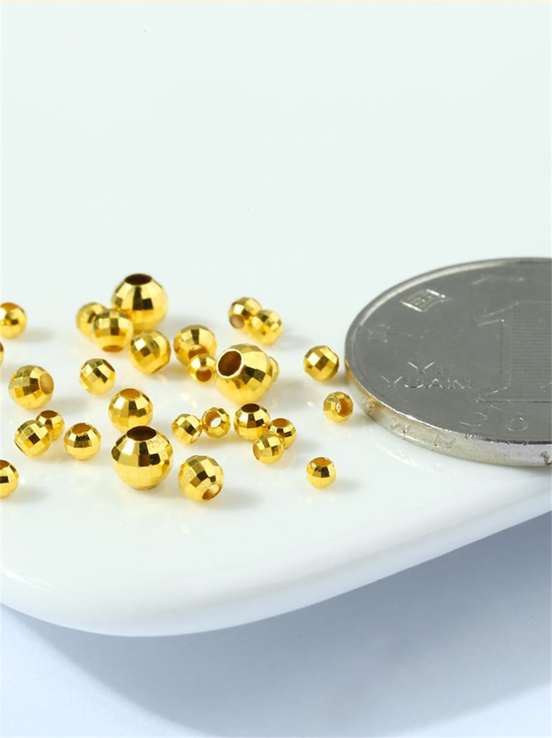 May include: A close-up of a group of small, gold-colored metal beads. The beads are faceted and have a hole in the center. A Chinese yuan coin is in the background for size reference.