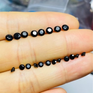 May include: A collection of black round gemstones of various sizes, displayed on a hand.