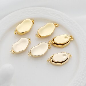 May include: Six gold-toned metal clasps for jewelry making. The clasps are shaped like a bean and have a smooth, polished finish.
