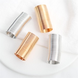 May include: Four metal spring coils in silver and gold tones. The coils are cylindrical with a ridged texture, and are arranged on a white surface. The gold coils have a warm, shiny appearance, while the silver coils have a cooler, metallic sheen.