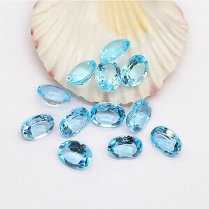 May include: A collection of oval-shaped, light blue gemstones. The gemstones are scattered on a white surface.