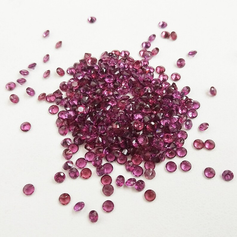 May include: A pile of small, round, pink gemstones. The gemstones are scattered on a white surface.