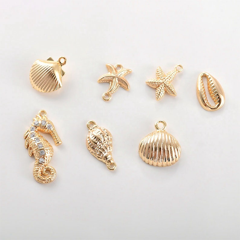 May include: Gold-toned metal charms with a nautical theme. The charms include a seashell, a starfish, a seahorse, and a conch shell.