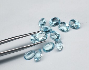 May include: A collection of oval-shaped, light blue gemstones, some of which are being held by a pair of tweezers.
