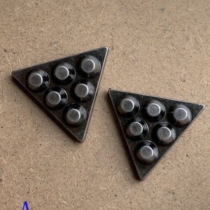 May include: Two silver triangle-shaped metal pieces with six round black metal accents on each piece.