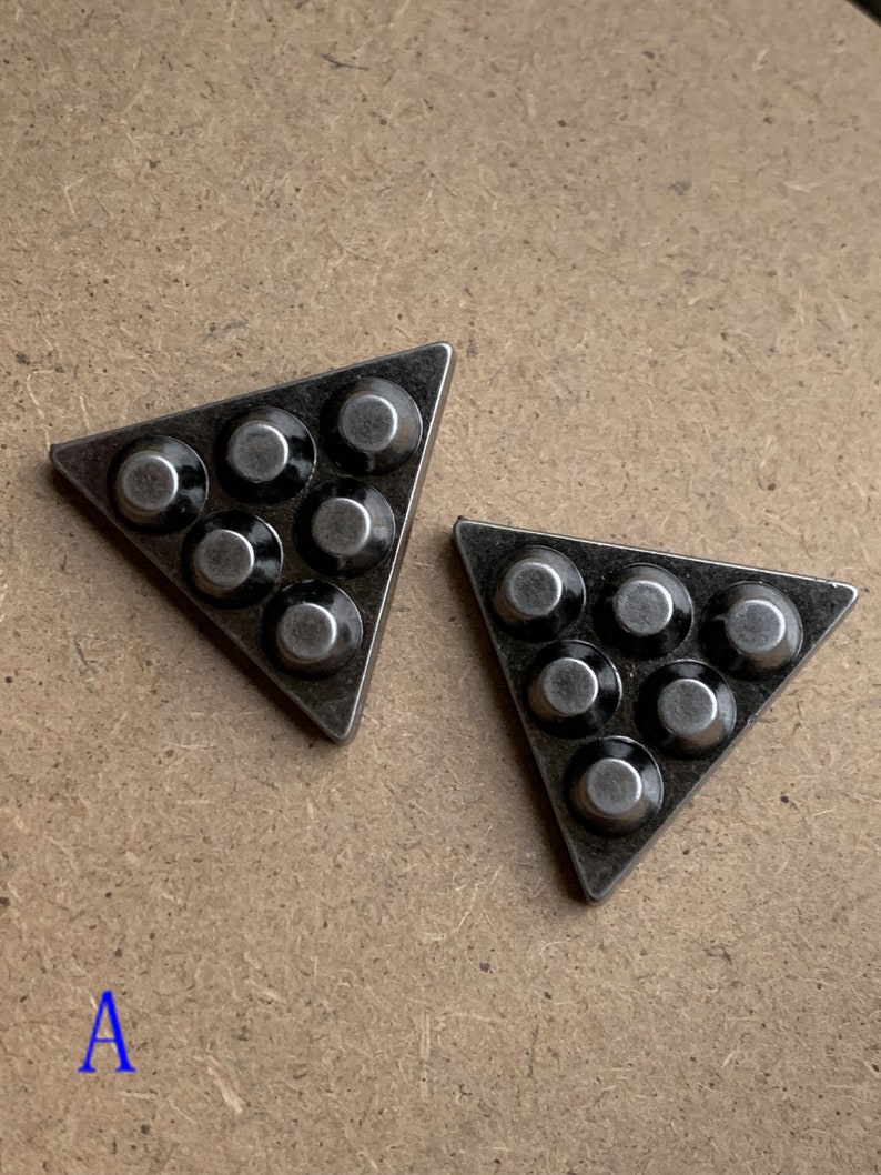 May include: Two silver triangle-shaped metal pieces with six round black metal accents on each piece.