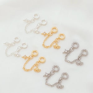 May include: A collection of gold and silver-toned charm connectors. Each connector features a chain with a star or leaf charm, and a ring on each end. The charms are designed for jewelry making.
