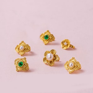 Puede incluir: Seis pendientes de tono dorado con diseños intrincados. Algunos pendientes presentan una piedra preciosa verde, mientras que otros presentan una perla blanca.