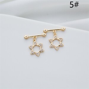 May include: A pair of gold-tone jewelry connectors with a star-shaped charm. Each connector has a bar with small flower-shaped accents and a dangling star charm with clear rhinestones.
