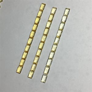 Peut inclure: Trois rangées de pierres précieuses rectangulaires, facettées et jaunes. Les pierres précieuses sont disposées en ligne droite, chaque rangée étant légèrement décalée par rapport à celle du dessus.