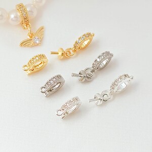 May include: A collection of gold and silver-toned jewelry findings, including earring components and clasps. Some pieces are adorned with small, clear gemstones. One earring features a wing charm with a central stone. The findings are displayed on a white surface.