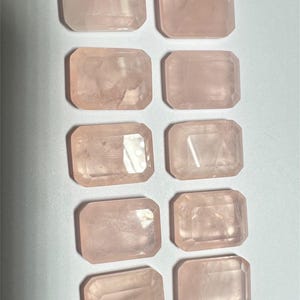 May include: Ten pink rose quartz stones, each cut into a rectangular shape with beveled edges. The stones are arranged in two rows of five, with the top row slightly offset from the bottom row.