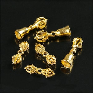 May include: Six gold-colored metal charms in the shape of a bell with a decorative top. The charms are intricately detailed and have a traditional design.
