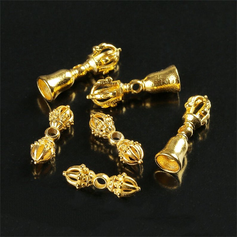 May include: Six gold-colored metal charms in the shape of a bell with a decorative top. The charms are intricately detailed and have a traditional design.