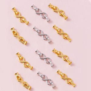 May include: A collection of jewelry clasps arranged in rows, featuring an infinity symbol design. The set includes several gold-toned metal clasps and a smaller number of silver-toned metal clasps, each with small end caps for attaching to jewelry cords.