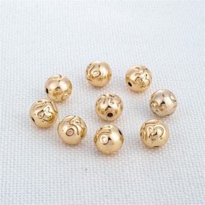 Puede incluir: Diez cuentas redondas de color dorado con un patrón decorativo. Las cuentas miden aproximadamente 1 cm de diámetro.