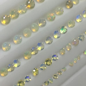 May include: Rows of faceted opal gemstones in various sizes. The opals display a range of colors, including white, yellow, and iridescent flashes of blue and green. The gemstones are arranged in a white tray.