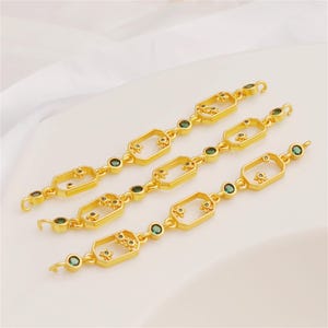 Può includere: Tre connettori per catena in metallo dorato con cornici rettangolari aperte, piccoli dettagli a forma di fiore e pietre rotonde incastonate di colore verde scuro. Ogni pezzo presenta un piccolo gancio su entrambe le estremità per gioielli.