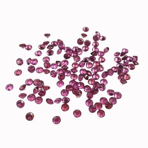 May include: A scattering of small, round, pink gemstones. The gemstones are faceted and have a shiny, polished finish.