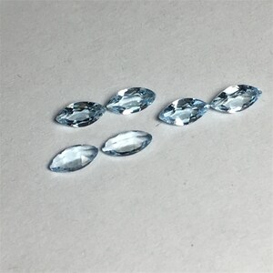 May include: Six light blue marquise-shaped gemstones on a white surface.
