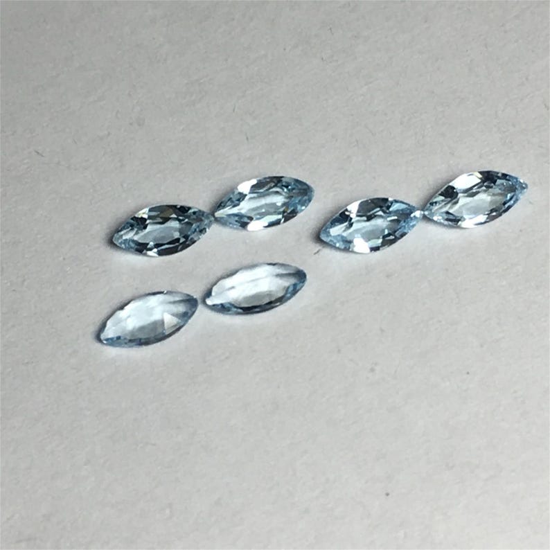 May include: Six light blue marquise-shaped gemstones on a white surface.