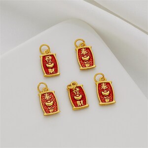 May include: Five rectangular gold-toned metal charms featuring a red enamel background with a textured pattern. Each charm displays raised gold Chinese characters and a small gold ingot symbol in the center, topped with a circular jump ring.