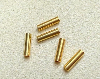 May include: Five small, cylindrical, gold-colored metal tube beads arranged in a scattered pattern. Each bead features a smooth, polished surface with a hollow center, designed for threading onto string or wire for jewelry making projects.