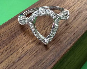 May include: A silver ring with a pear-shaped setting surrounded by small diamonds. The ring is set on a wooden surface.