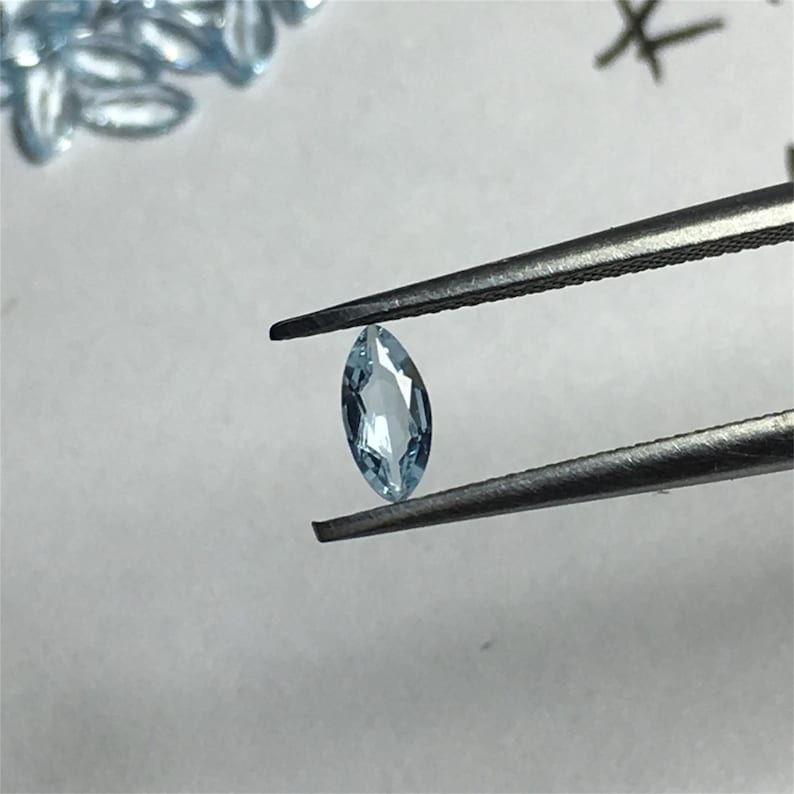 May include: A light blue marquise-shaped gemstone held by tweezers.