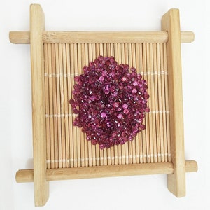 May include: A pile of small, faceted, pink gemstones in a round shape on a bamboo mat.