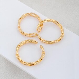 May include: Three gold-colored chain link rings. The rings are open-ended, allowing them to be adjusted. The jewelry is displayed on a white surface. The rings are made of a shiny, metallic material.