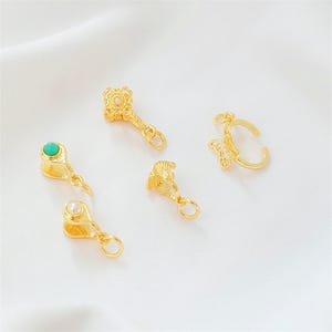 Puede incluir: Un surtido de dijes de joyería dorados. Los dijes incluyen una llave, un anillo de mariposa y dijes en forma de lágrima con una perla y una piedra turquesa. Cada dije tiene un pequeño lazo para sujetarlo a un collar o pulsera.