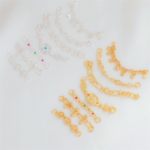 May include: A collection of silver-toned and gold-toned metal jewelry connectors and chain extenders. These decorative pieces feature intricate filigree patterns, small dangling charms, and embedded colorful rhinestones in red, green, and blue.
