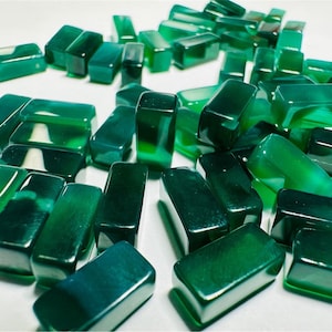 May include: A collection of green, translucent, rectangular glass stones. The stones have a mottled, marbled appearance.
