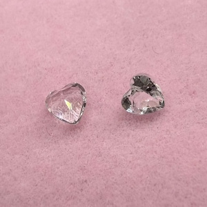 Puede incluir: Dos cristales transparentes en forma de corazón sobre un fondo rosa.