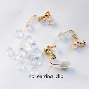 Könnte beinhalten: Drei goldfarbene Schraub-Ohrclips aus Metall mit transparenten Silikonpolstern und eine Sammlung loser, runder, transparenter Silikon-Ohrring-Puffer. Ein roter Pfeil zeigt auf einen der Ohrclips mit dem Text no earring clip.