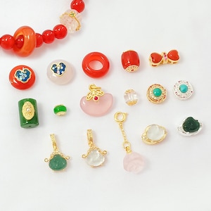May include: A collection of colorful beads and charms in various shapes and sizes. Includes red, green, pink, and gold-toned pieces. Some beads have intricate designs, and others are simple. Ideal for jewelry making or crafting.