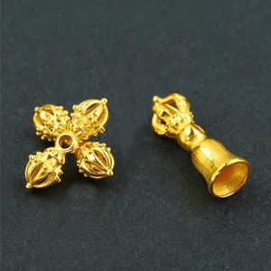May include: Two gold-colored metal charms, one shaped like a bell with a decorative top and the other shaped like a four-pointed star with decorative balls at each point.
