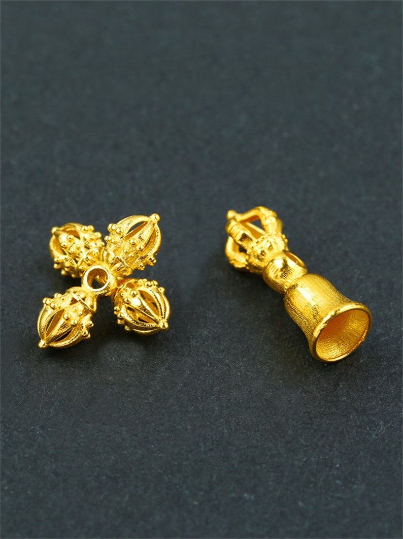 May include: Two gold-colored metal charms, one shaped like a bell with a decorative top and the other shaped like a four-pointed star with decorative balls at each point.
