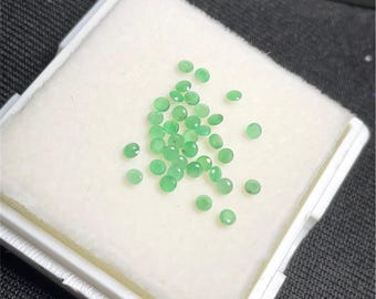 May include: A small white box with a white foam insert containing a collection of round, green gemstones.