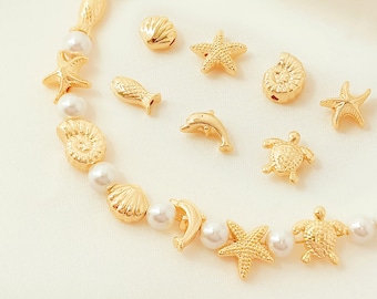 May include: A necklace featuring a strand of white pearls interspersed with gold-colored sea-themed charms. The charms include starfish, seashells, a dolphin, a fish, and a turtle. The necklace is displayed on a white surface.