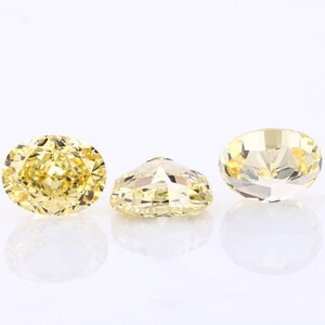 May include: Three oval-shaped, faceted, yellow gemstones. The gemstones are set on a white background.