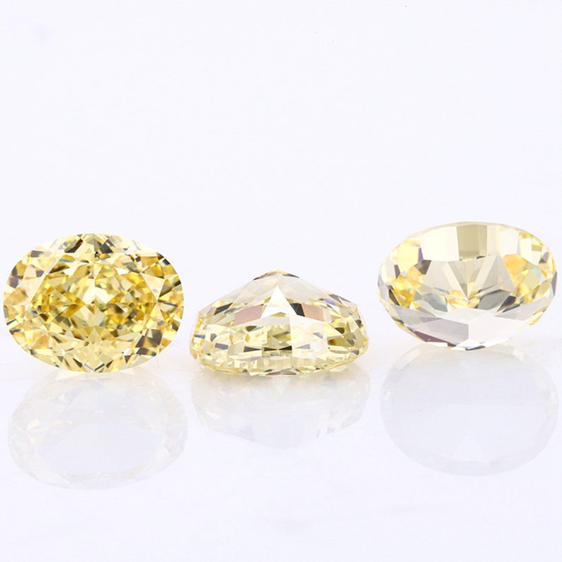 May include: Three oval-shaped, faceted, yellow gemstones. The gemstones are set on a white background.