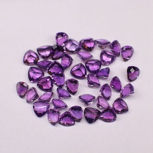 Puede incluir: Una colección de piedras preciosas de amatista, talladas en forma triangular con una punta puntiaguda. Las piedras son de color púrpura intenso y tienen un acabado brillante.