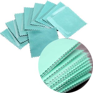 Puede incluir: Un conjunto de pequeños paños de limpieza rectangulares de color turquesa con un borde dentado. Los paños están empaquetados individualmente en plástico transparente. Un primer plano muestra la textura y los detalles de los paños.