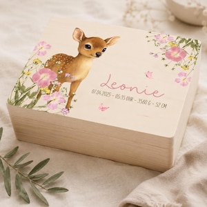May include: A rectangular light-coloured wooden keepsake box featuring a printed illustration of a fawn surrounded by pink and yellow wildflowers. The lid displays the name Leonie in pink script, followed by the text 07.04.2025 - 05:35 UHR - 3580 G - 52 CM.