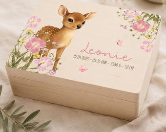 May include: A rectangular light-colored wooden keepsake box featuring a printed illustration of a fawn surrounded by pink and yellow wildflowers. The lid displays the name Leonie in pink script, followed by the text 07.04.2025 - 05:35 UHR - 3580 G - 52 CM.